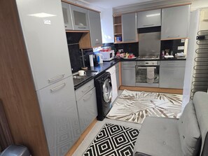 Una cucina compatta con mobili grigi, una lavatrice, un forno a microonde e un piano cottura.