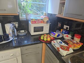 Una cocina con microondas, cafetera y diversos alimentos sobre la encimera.