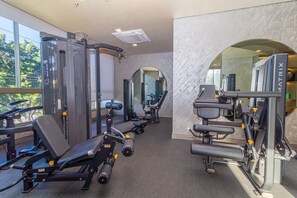 Et fitnessrum med forskellig træningsudstyr, et spejl og udsigt til træer gennem store vinduer.