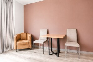 Ein Zimmer mit hellem Holzboden, einem braunen Ledersofa, einem kleinen Holztisch mit Metallbeinen und zwei passenden Stühlen.