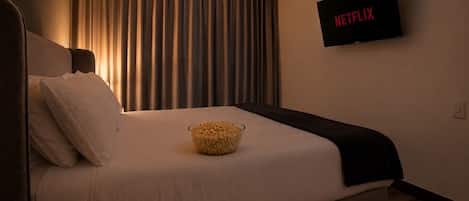 Ein Hotelzimmer mit einem Bett, einer Portion Popcorn, einem Fernseher mit 'NETFLIX' und einem Vorhang.