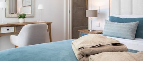 A hotel room with a bed, bedside table, lamp, and a desk with a chair.