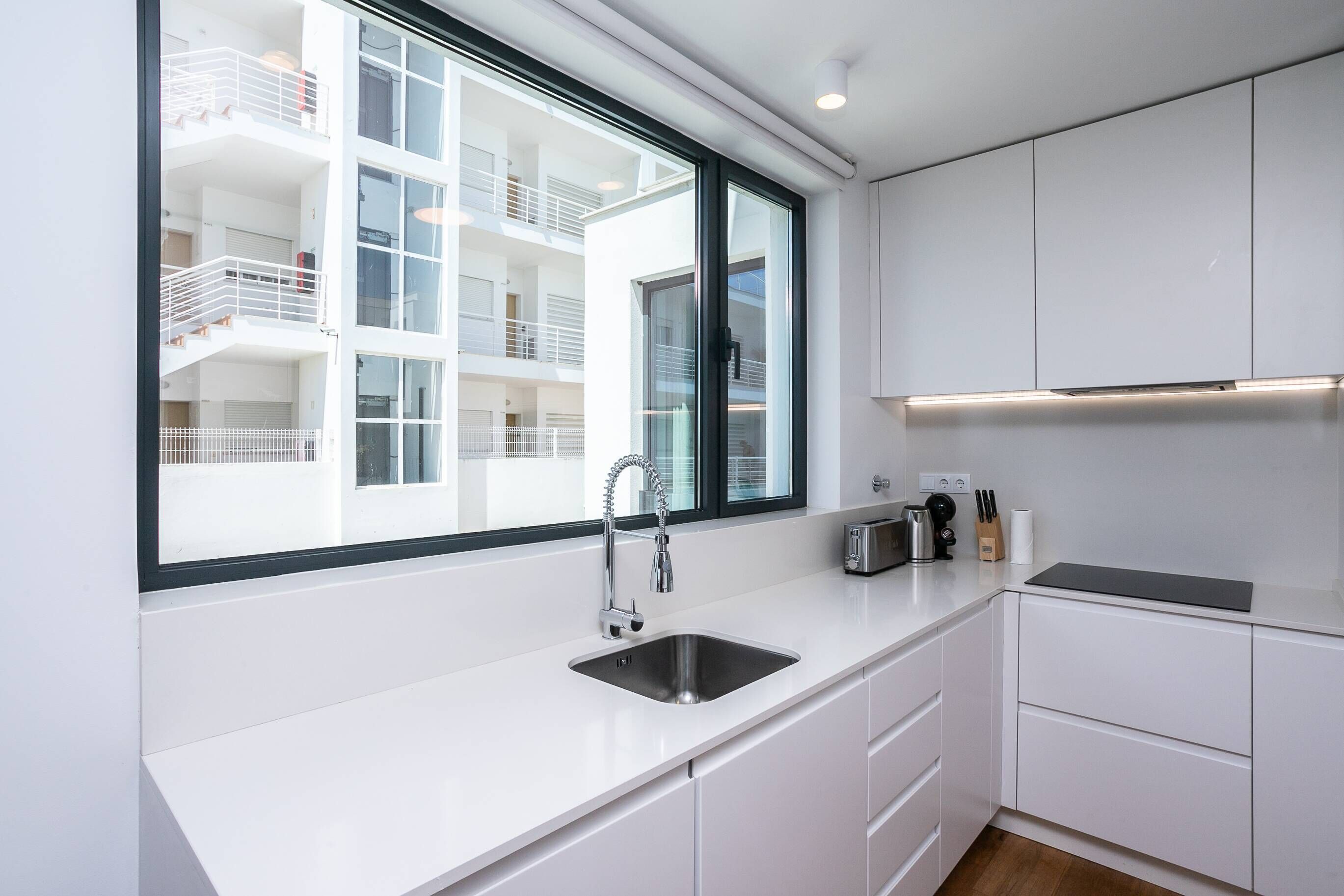 A modern kitchen with a large window, white cabinetry, and a stainless steel sink.