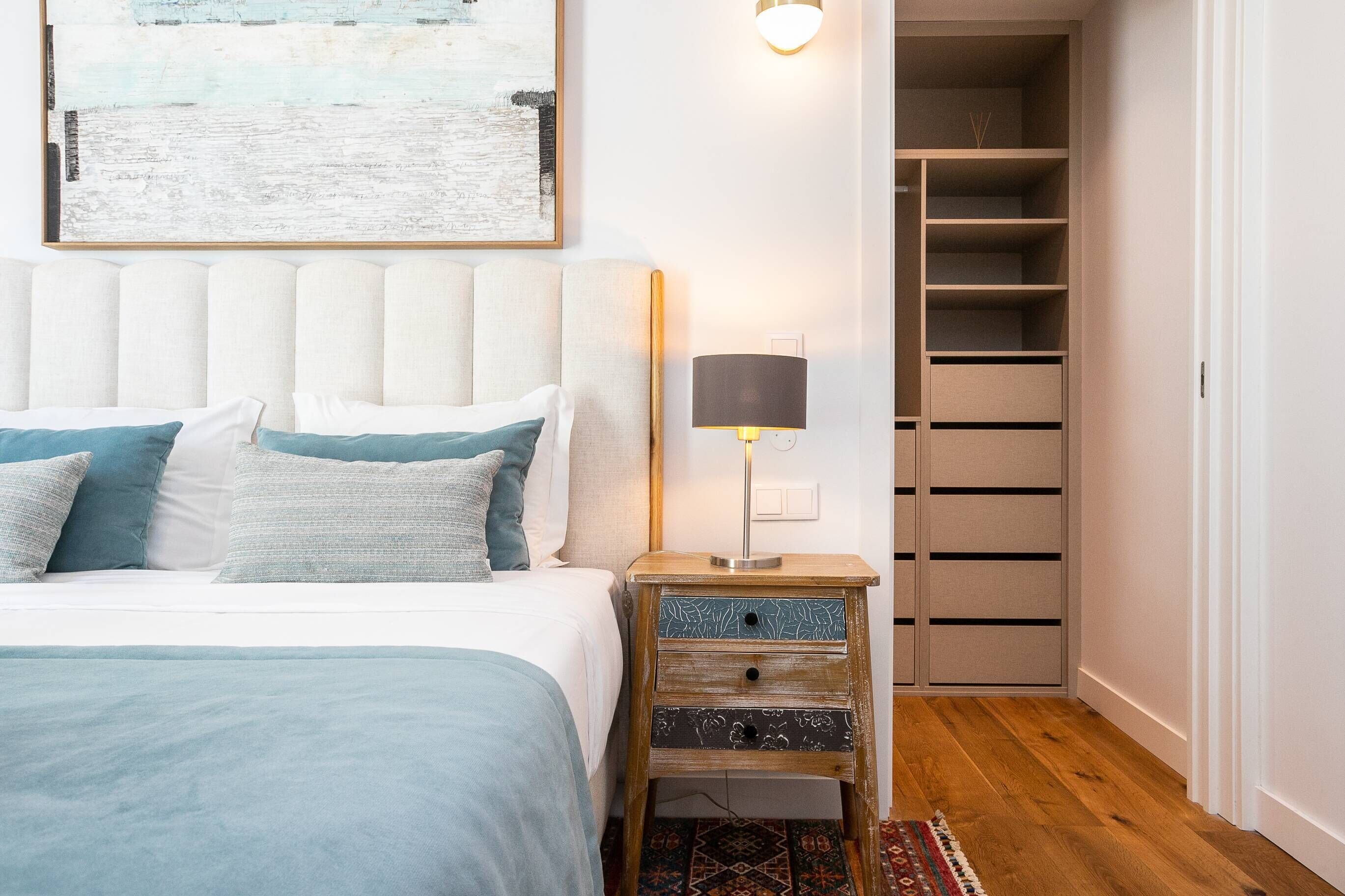 A bedroom with a bed, bedside table, lamp, and a closet with shelves.