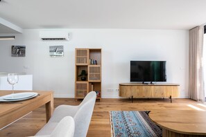 Ein modernes Wohnzimmer mit einem Holzesstisch, einer Couch, einem Fernseher auf einem Holzboden und einem Bücherregal.