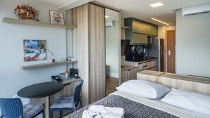 Ett hotellrum med en säng, ett skrivbord, en stol, ett litet bord, ett litet kök och ett badrum.