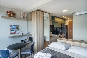 Ein Hotelzimmer mit Bett, Schreibtisch, Stuhl, kleinem Tisch, Küchenzeile und Bad.