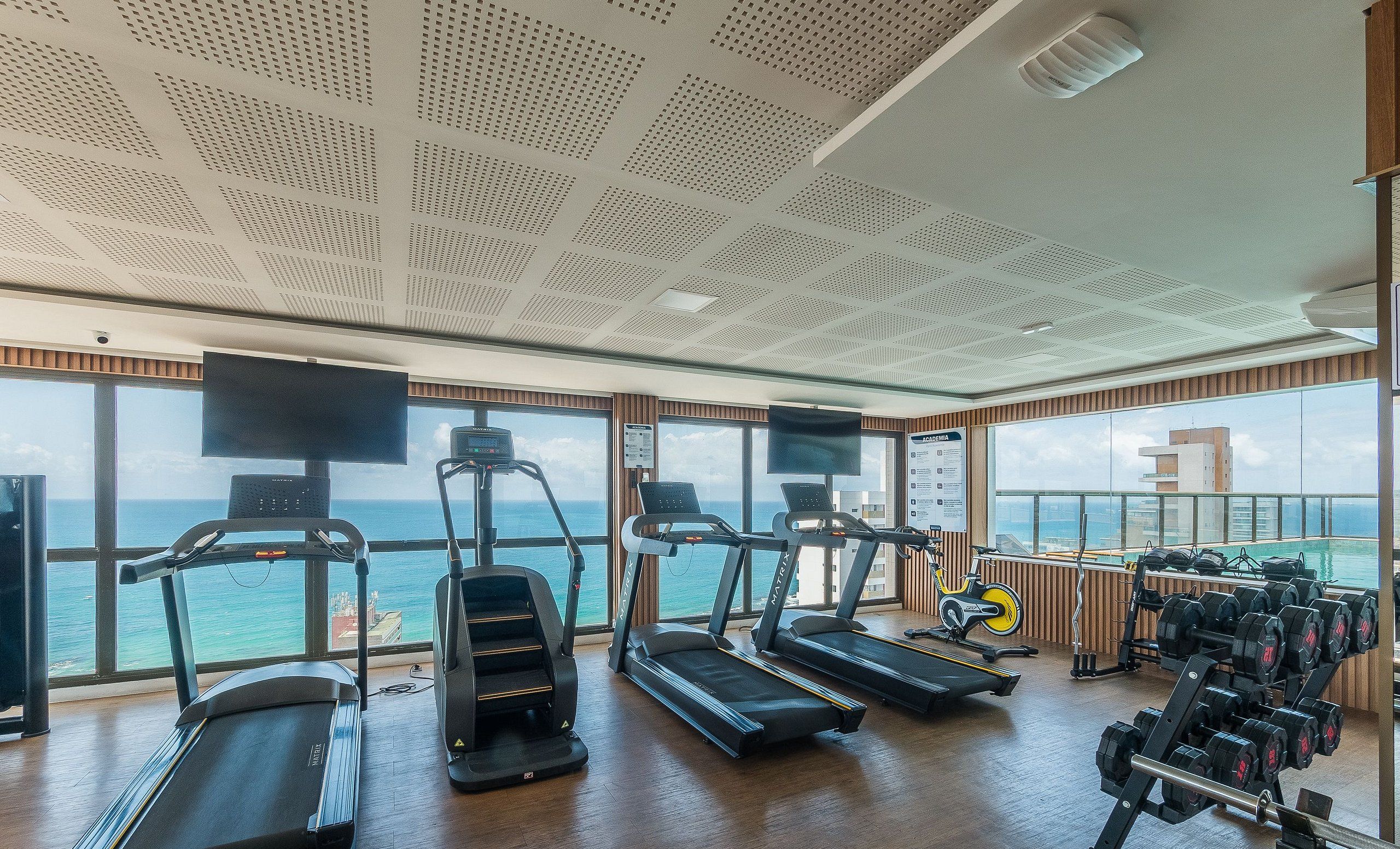 A gym with treadmills, stationary bikes, and weight machines, overlooking a body of water.