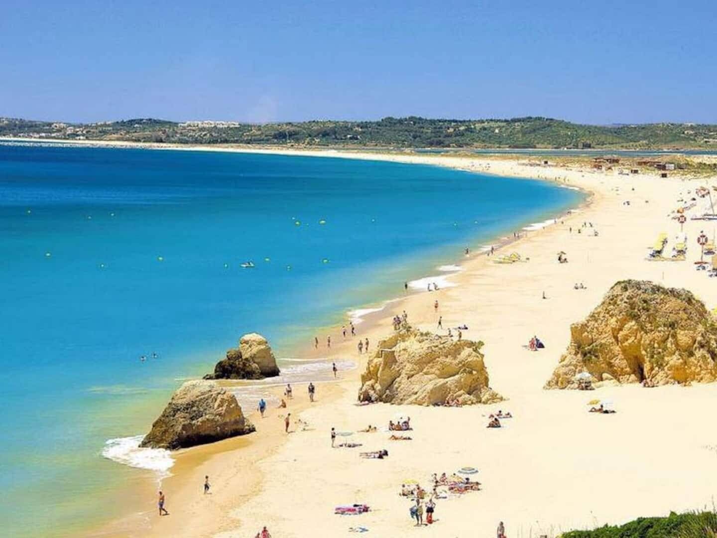 A beach with clear blue water, sandy shore, and rocky outcrops.