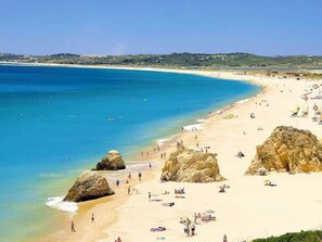 Ein Strand mit klarem, blauem Wasser, sandigem Ufer und Felsen.