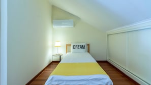 Una camera d'albergo con un letto, una lampada da comodino, un cuscino con la scritta 'DREAM' e un condizionatore d'aria.