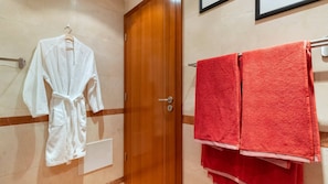 Een badkamer met een houten deur, een witte badjas hangend aan een rek, en twee rode handdoeken op een handdoekrek.