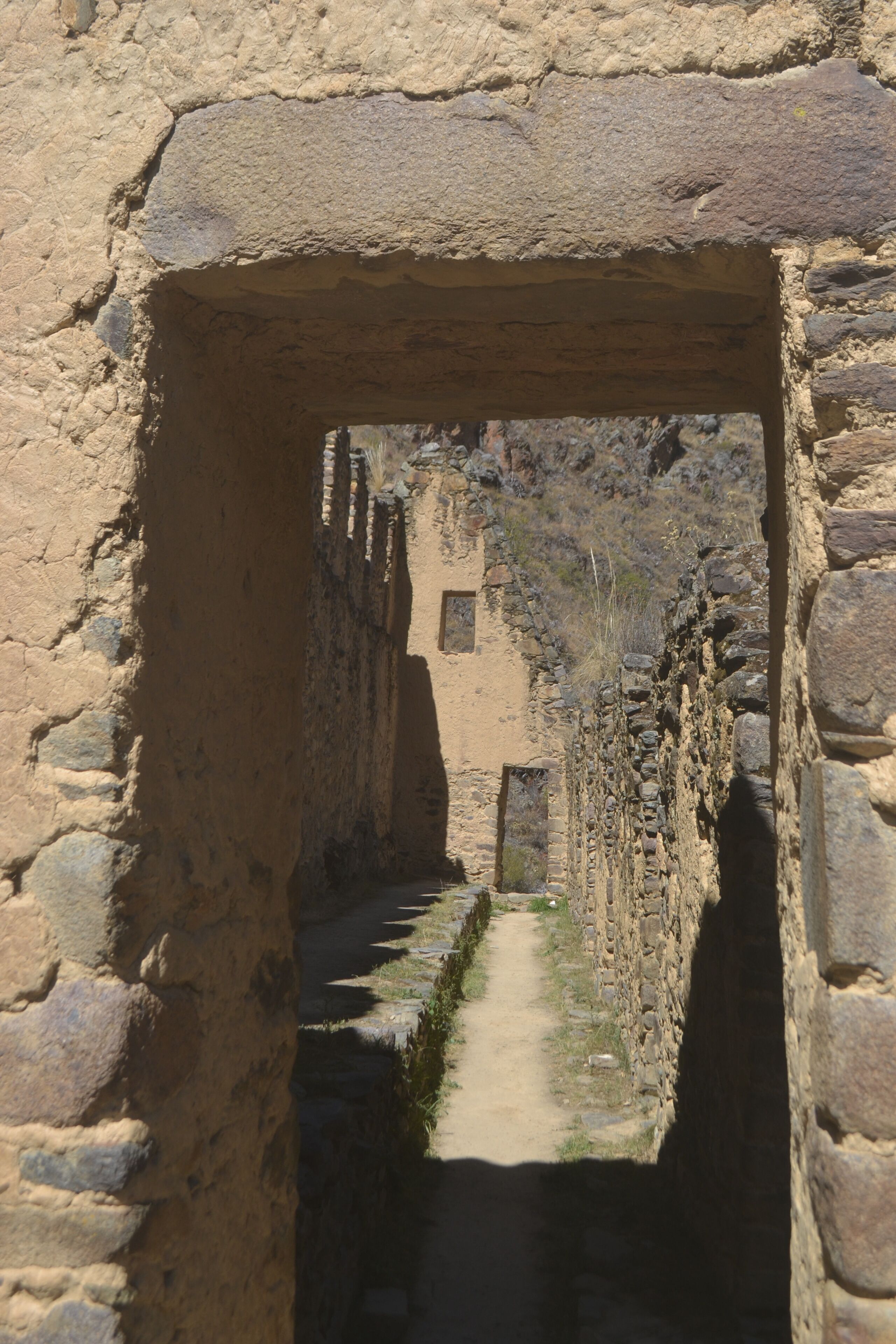A narrow stone pathway leading through an arched doorway, flanked by stone walls.
