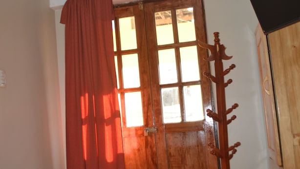 A room with a bed, a wooden wardrobe, a window with curtains, and a television on a stand.