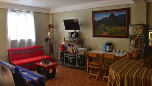 Un salon avec un canapé rouge, un téléviseur, une table à manger avec des chaises et une bibliothèque.