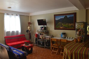 A living room with a red sofa, a television, a dining table with chairs, and a bookshelf. - PUMAMARKA HOUSE OLLANTAYTAMBO (Ollantaytambo)