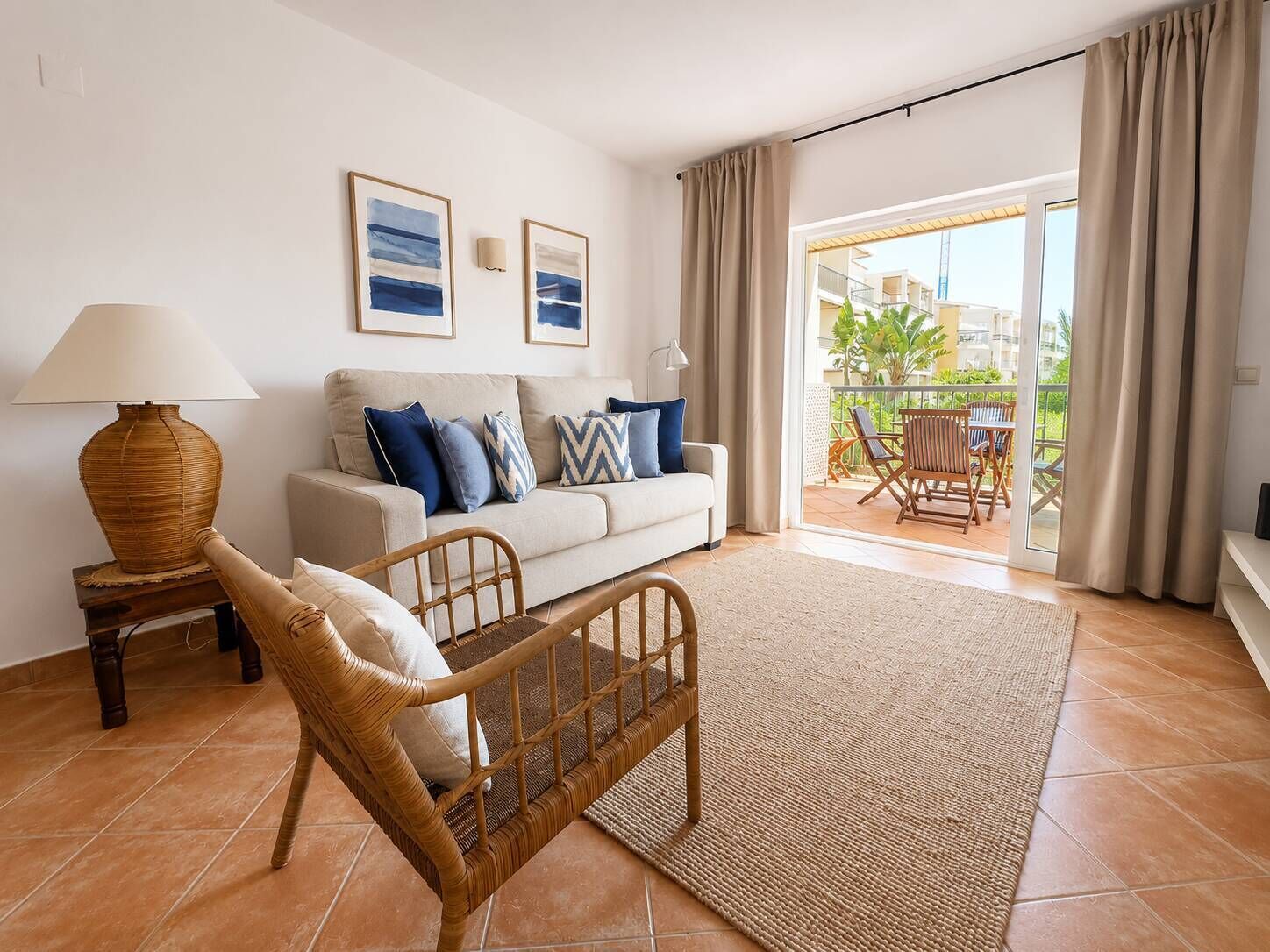 A living room with a sofa, a wicker chair, a lamp, and a view of the outside balcony.
