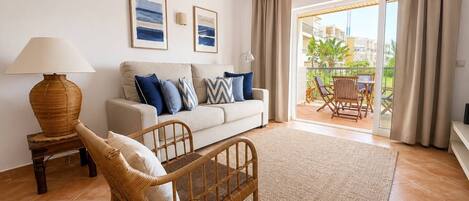 A living room with a sofa, a wicker chair, a lamp, and a view of the outside balcony.