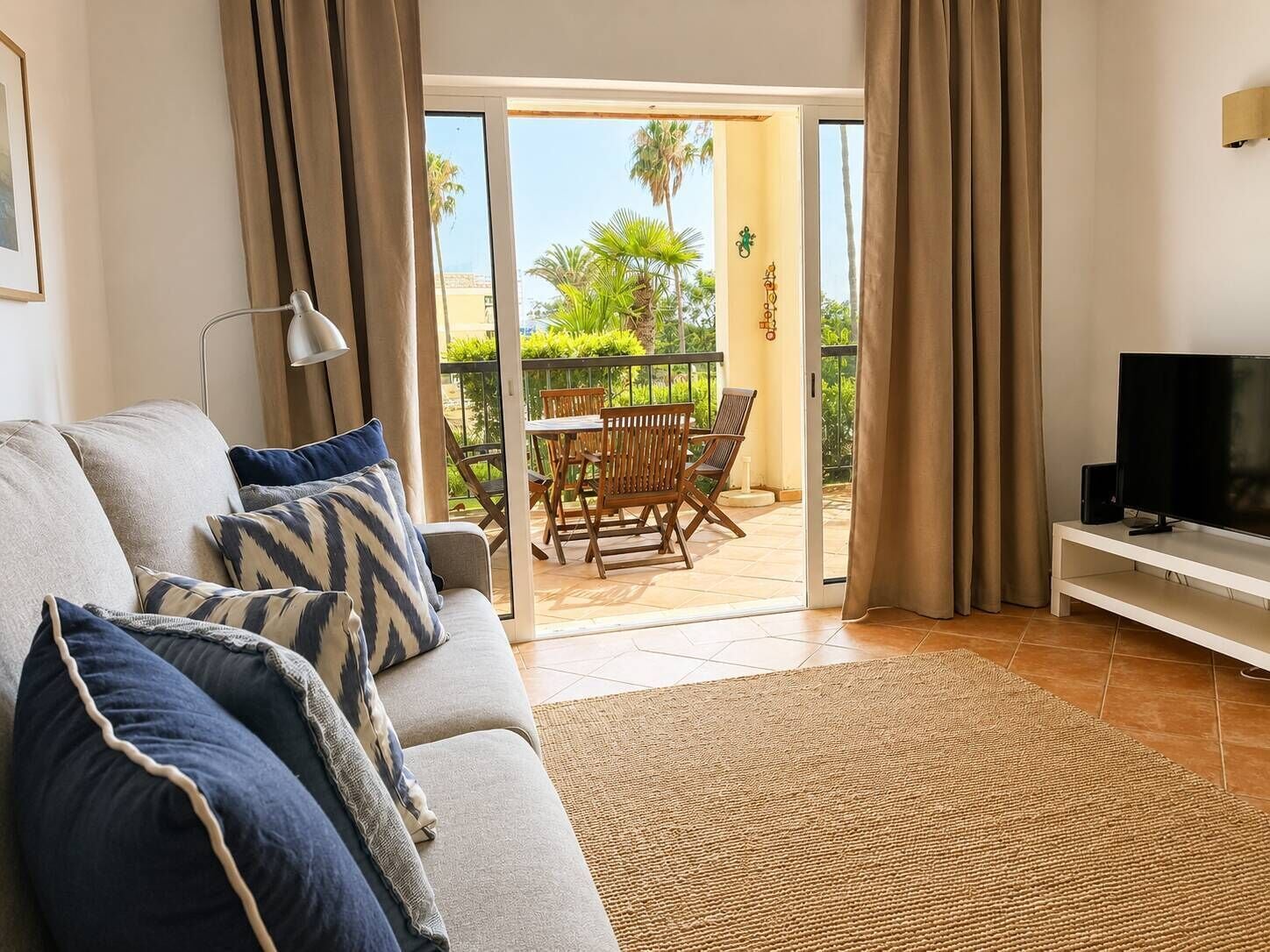 A living room with a sofa, a television, and a view of an outdoor patio with a table and chairs.