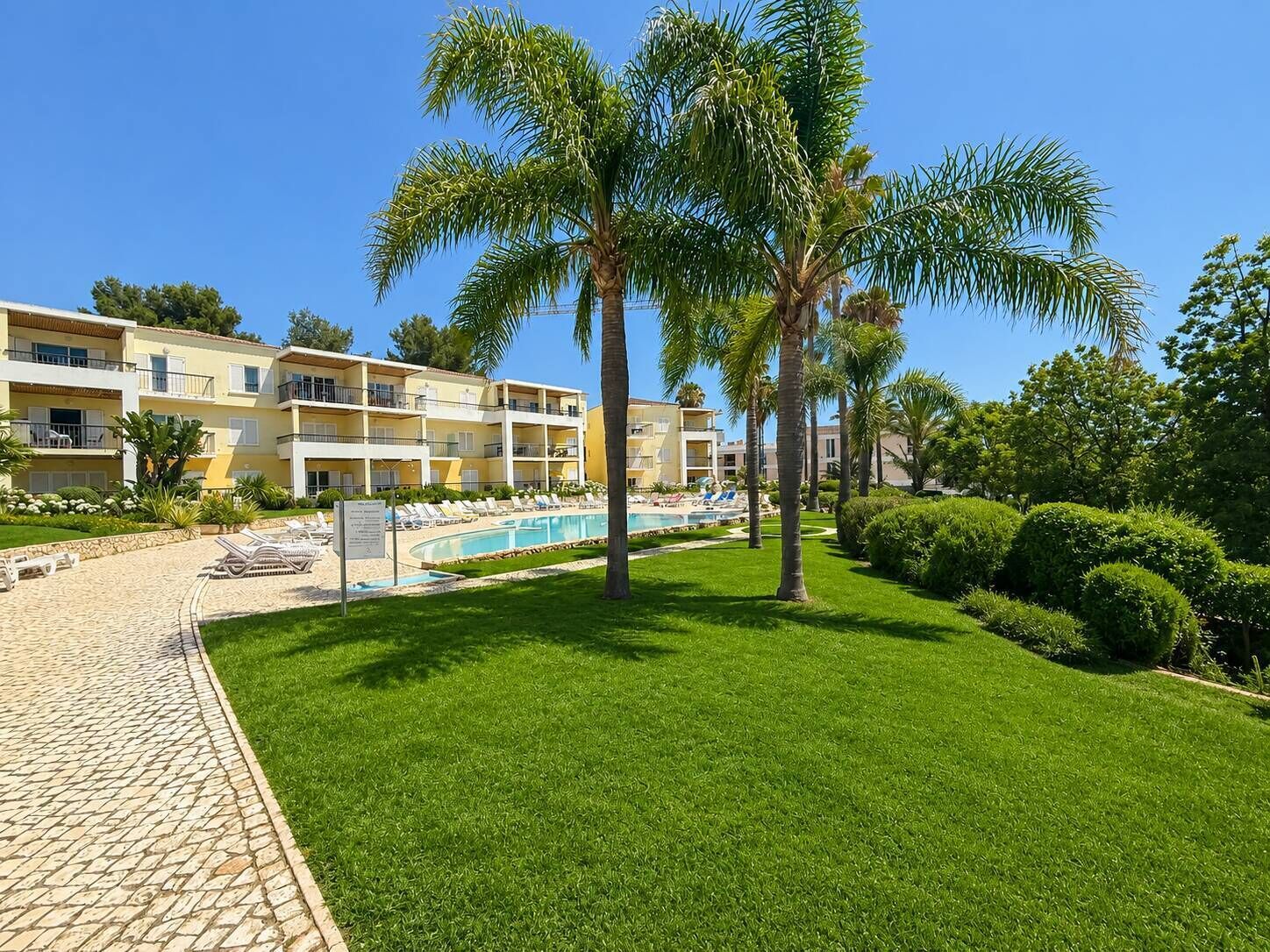 Un hotel amb piscina, palmeres i un jardí ben cuidat.
