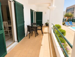A balcony with a table and chairs, a potted plant, and a view of a swimming pool with lounge chairs. - The Sea Breeze - Bright Beach Apartment - Centre (Portimão)