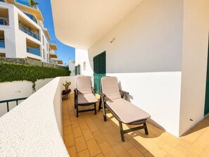 A balcony with two lounge chairs, a potted plant, and a white wall with a green shutter. - The Sea Breeze - Bright Beach Apartment - Centre (Portimão)