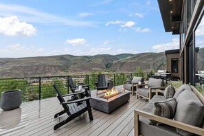 Eine Terrasse mit Gartenmöbeln, einem Feuerkorb und Blick auf ein Tal.