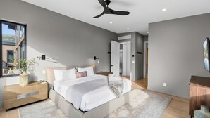 A modern bedroom with a bed, bedside tables, a nightstand, a ceiling fan, and a view of the outdoors. - EagleVail Designer Retreat | Sleeps 16 (Vail)