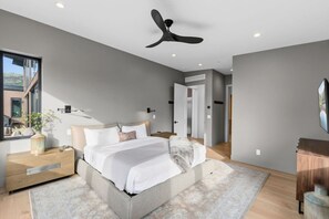 Ein modernes Schlafzimmer mit Bett, Nachttischen, Deckenventilator und Blick ins Freie.