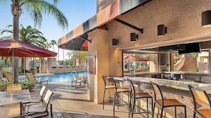 Zona de bar junto a la piscina con asientos exteriores y vistas al agua.