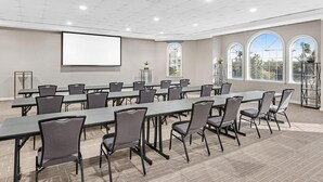 Une salle de conférence dotée de longues tables et de chaises, d’un écran de projection et de grandes fenêtres offrant une vue sur les palmiers.