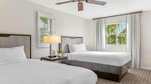 Une chambre d’hôtel avec deux lits, un ventilateur de plafond, une fenêtre avec des rideaux et une table de chevet avec une lampe.
