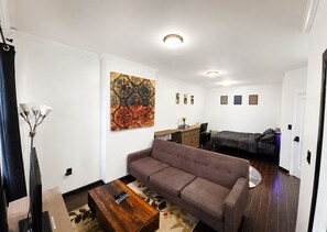 Ein Wohnzimmer mit Sofa, Couchtisch, Gemälde, Schreibtisch und Bett.