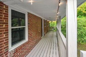 Eine überdachte Veranda mit Ziegelwand, weißen Geländern und einer Holzterrasse.