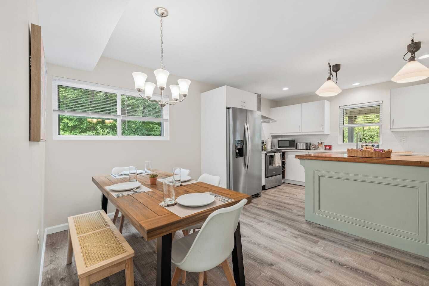 Une cuisine moderne avec un coin repas, comprenant une table en bois, des chaises blanches et un îlot central intégré avec un évier.