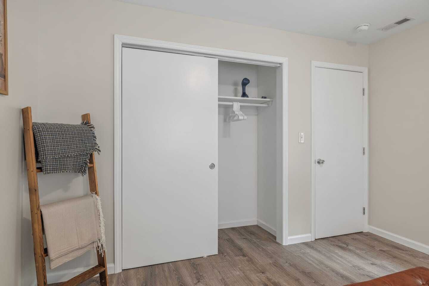 Una habitación con una escalera de madera, un armario blanco con repisa y una puerta cerrada.