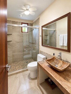 Een moderne badkamer met een douchecabine van glas, een wit toilet en een marmeren wastafel.