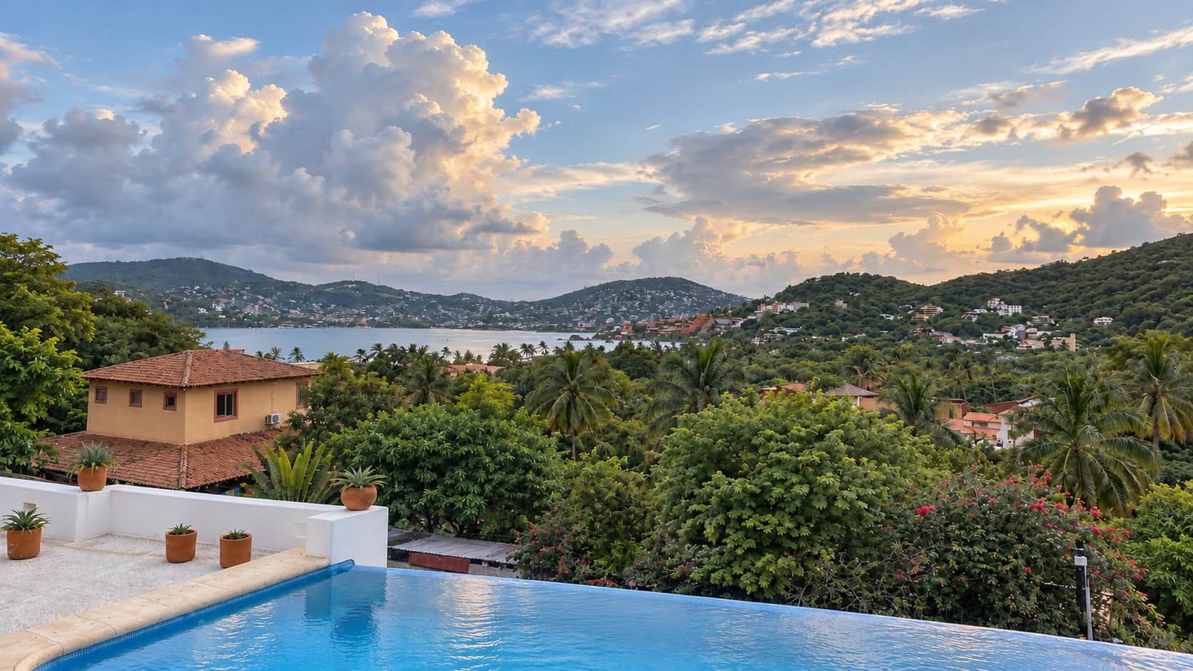 A pool with a view of a coastal town and hills.