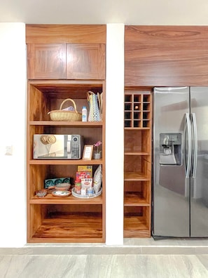A kitchen with a built-in wooden pantry, a stainless steel refrigerator, and various kitchen items on shelves. - Villa Violeta | Ocean Views Above Playa La Ropa (Zihuatanejo)