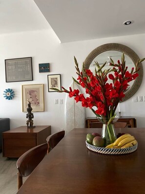 A dining area with a wooden table, chairs, a vase with red flowers, and a round mirror on the wall. - Villa Violeta | Ocean Views Above Playa La Ropa (Zihuatanejo)