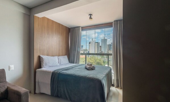 A hotel room with a bed, a view of the cityscape, and a window with curtains. - Apt 220m From the sea in a Condo w/ a Pool Bpm0909 (Salvador)