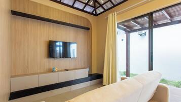 Una habitación de hotel moderna con un televisor de pantalla plana montado en una pared de madera, un sofá y un ventanal con cortinas.