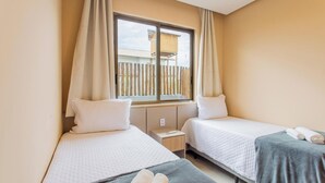 A hotel room with two beds, a window with curtains, a small bedside table, and a view of a wooden fence outside. - House by Lagoon, Near Beach Cdl0007 (Maraú)