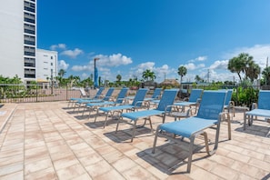 A rooftop pool area with blue lounge chairs and a white building in the background. - Sunset Condo #502 (Fort Myers Beach)