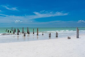 Ein Strand mit Holzpfählen und einem Leuchtturm in der Ferne.