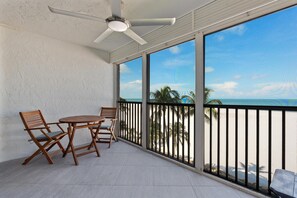 Ein Balkon mit Tisch und Stühlen, einem Deckenventilator und Blick auf den Strand.