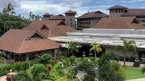 A resort with multiple buildings, including a central structure with a flat roof and smaller buildings with pitched roofs. There are outdoor seating areas with tables and chairs, surrounded by lush greenery and palm trees.
