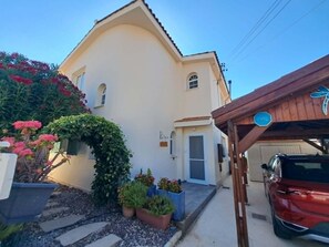 Ein zweistöckiges Gebäude mit weißer Fassade, eine Garage mit einem roten Auto und ein überdachter Bereich mit einem blauen Schild.