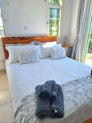 Ein Bett mit weißer Bettwäsche und einer gemusterten Tagesdecke, ein Holz-Kopfbrett und ein Fenster mit Vorhängen.