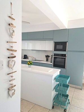 A modern kitchen with white cabinets, a central island, a microwave, an oven, and a teal cart. - Villa Ella - peaceful detached villa close to beach and mountains - Sleeps 6 (Argaka)